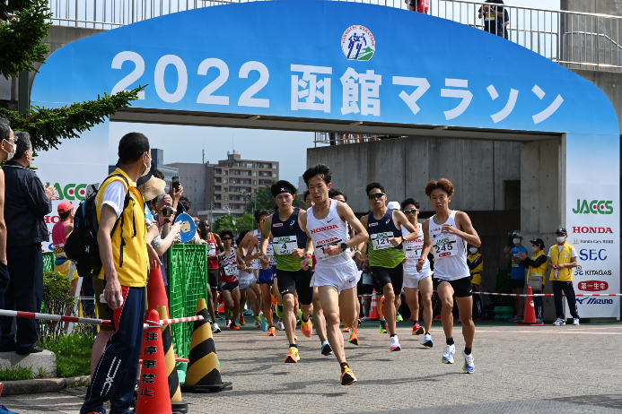 競技場からコースへ出るハーフマラソンの選手たち